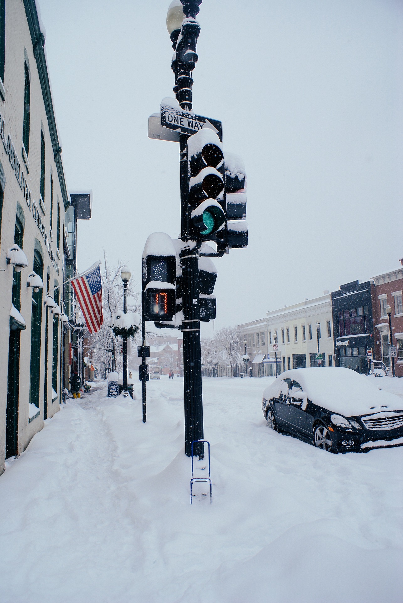 snow storm in a US town covering the ground, buildings, traffic light, and a car